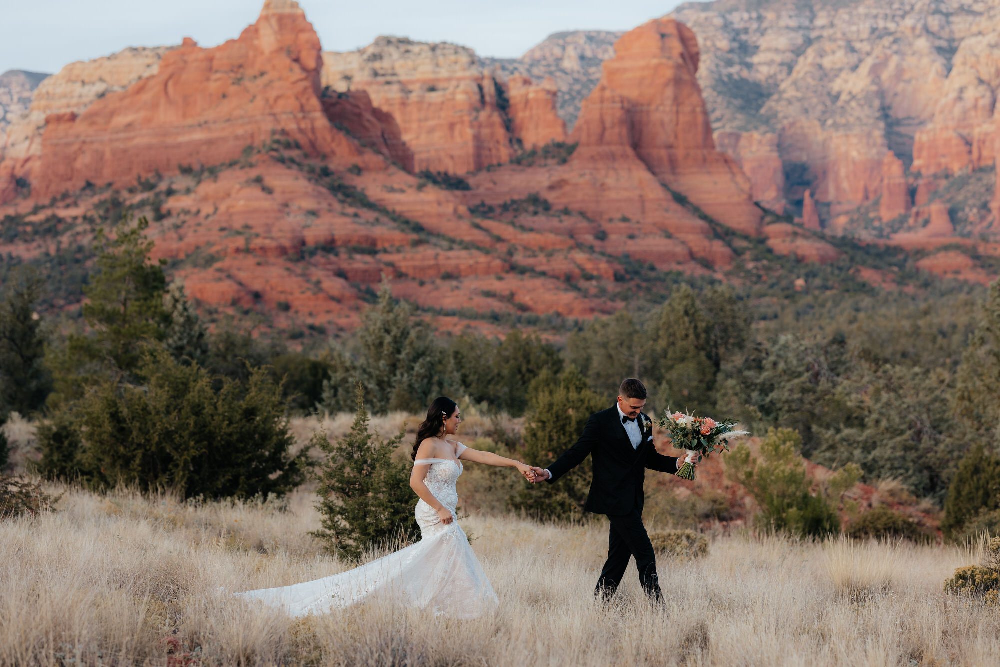 Married couple walking through field with Sedona mountain backdrop